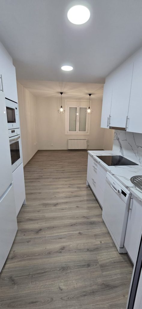 Cocina blanca a medida con encimera de mármol y suelo de madera en Vigo